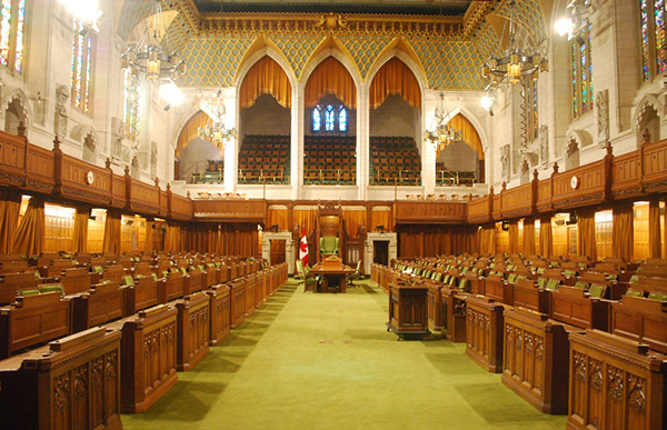 Interior of the Canadian House of Commons, parliament assembly room with green carpet, wooden benches and stained glass windows