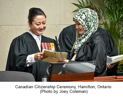 Canadian Citizenship Ceremony, Hamilton, Ontario woman receiving citizen document from woman in black robe with medals