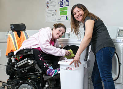 Two smiling women doing laundry, one in a wheelchair and one standing