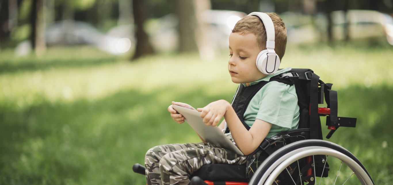 Young boy in a manual wheelchair using a tablet while listening with headphones