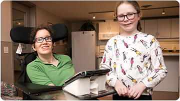 Smiling daughter standing beside her smiling mother in an electric wheelchair