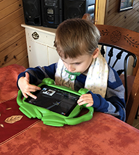 Child sitting at a table using a green tablet